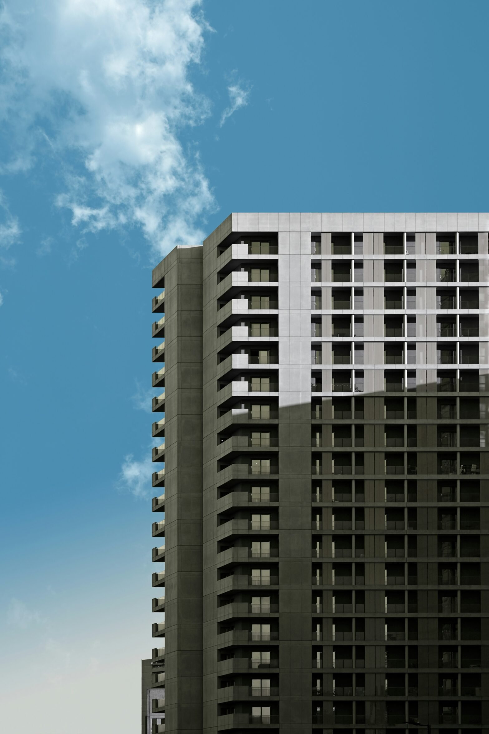 Modern high-rise apartment building against a clear blue sky with clouds.