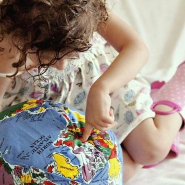 A young child exploring a plush globe while sitting on a bed, showcasing curiosity and learning.