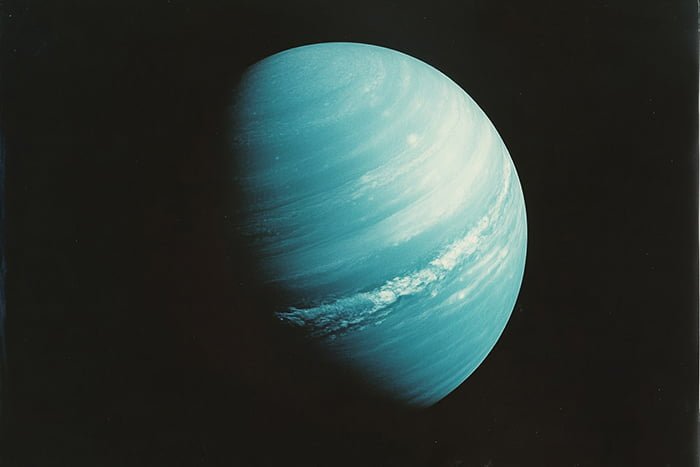 A blue-green planet with visible cloud bands, partially illuminated against a dark background — Uranus in all its serene beauty.