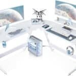 A white L-shaped computer desk setup with two monitors, a mechanical keyboard, a mouse, a computer tower, a model figure, a gaming console controller, headphones, and various accessories.