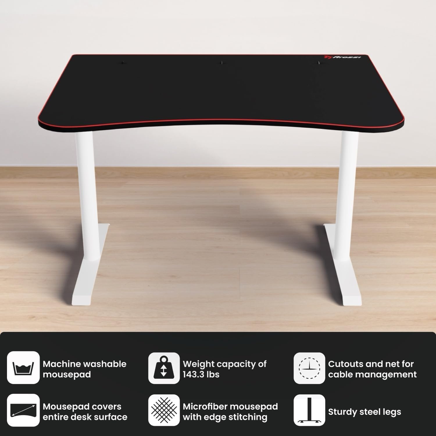 A black-top desk with white legs stands on a wooden floor. Icons below highlight machine washable mousepad, 143.3 lbs weight capacity, cable management cutouts, edge-stitched microfiber mousepad, and sturdy steel legs.