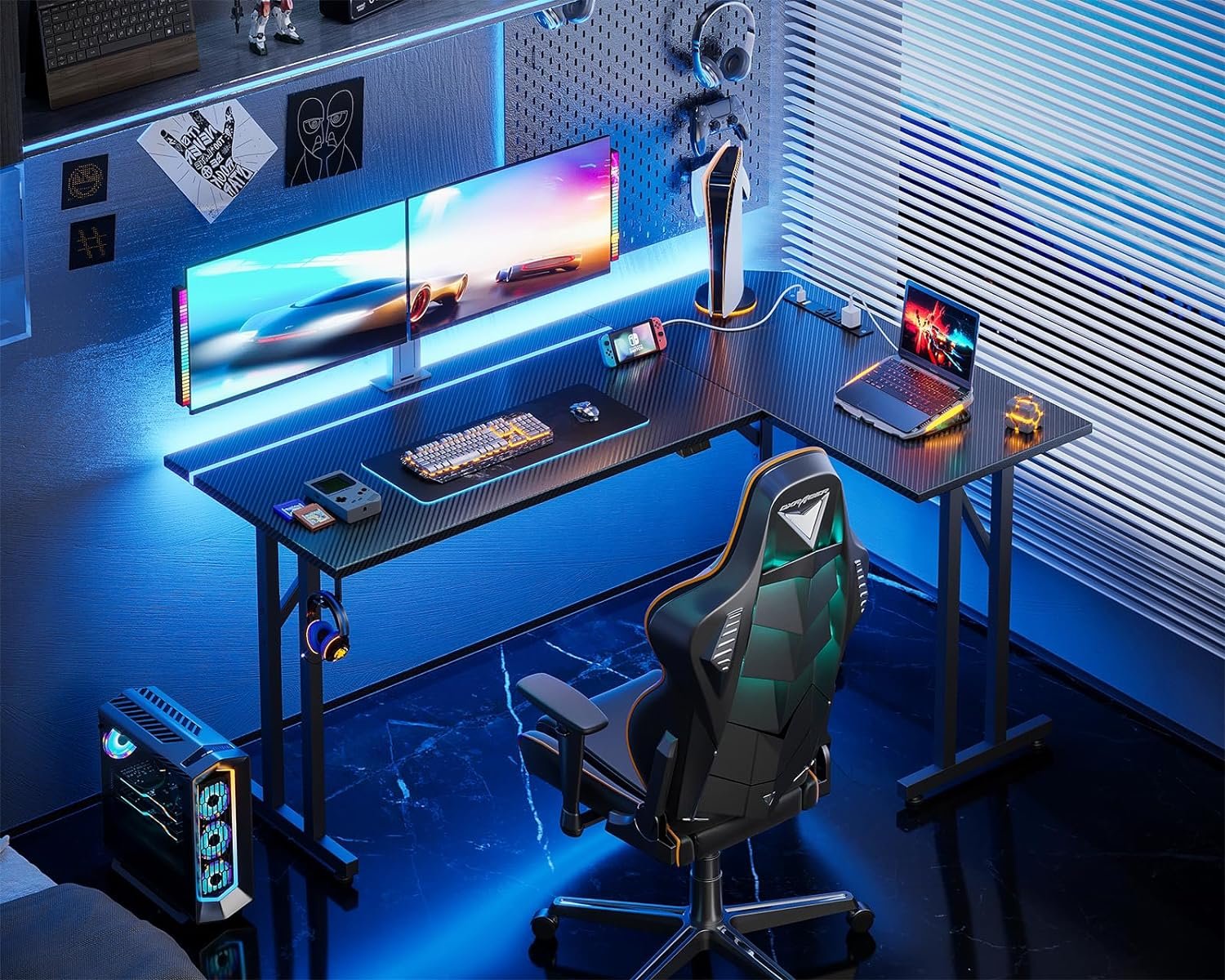 A sleek, modern gaming setup with dual monitors, a gaming chair, RGB lighting, a keyboard, mouse, laptop, and gaming PC on a carbon-fiber desk, against a blue-toned room with blinds.