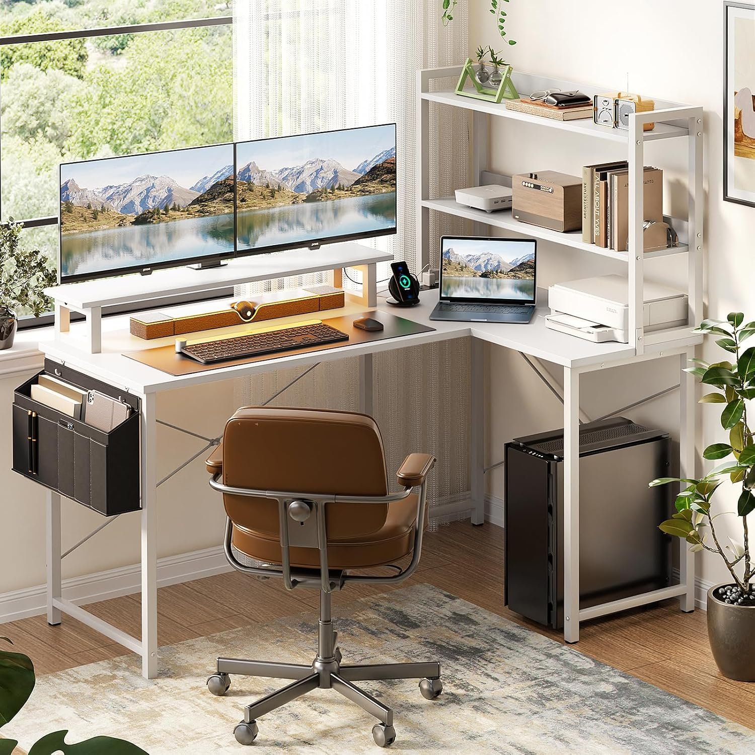 A modern home office setup features a white L-shaped desk with dual monitors displaying a mountain landscape, a brown leather chair, shelves with decor and office supplies, and a mini fridge underneath.