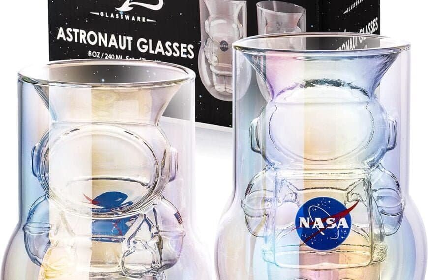 Two astronaut-themed glasses are displayed in front of their packaging. The glasses feature an astronaut-shaped design inside and have NASA and a spaceship logos. The packaging is branded "Dragons Glassware.