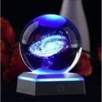 A glowing 3D galaxy hologram inside a crystal ball on a lit base, with a dark background.