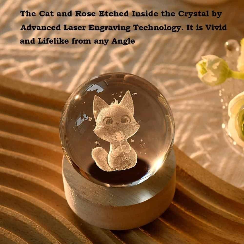 A crystal orb with an etched image of a cat holding a rose, placed on a wooden stand, with text describing the laser engraving technology.