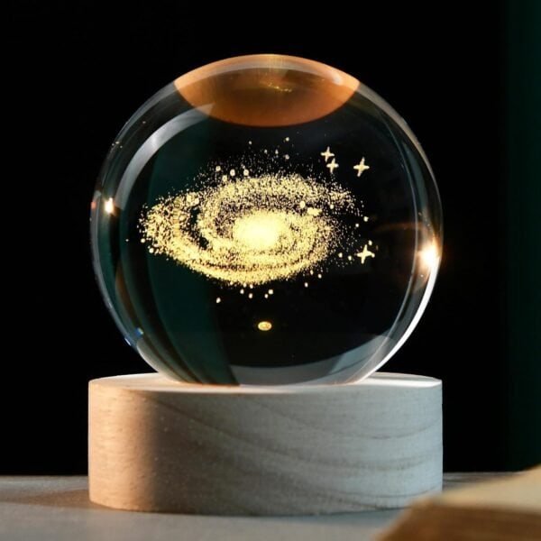 Glass orb with a galaxy design inside, resting on a wooden base against a dark background.