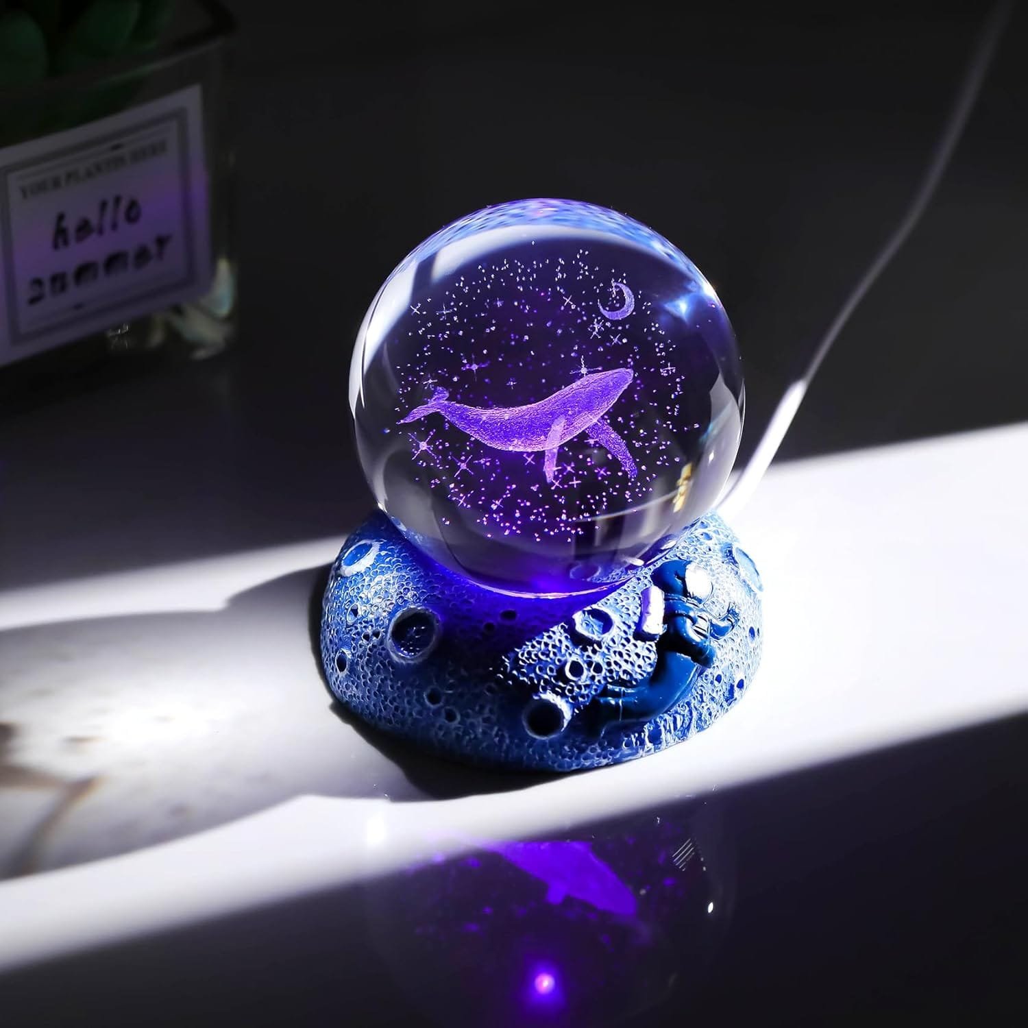 A glass ball with a holographic whale projection sits on a textured blue base, illuminated against a dark background.