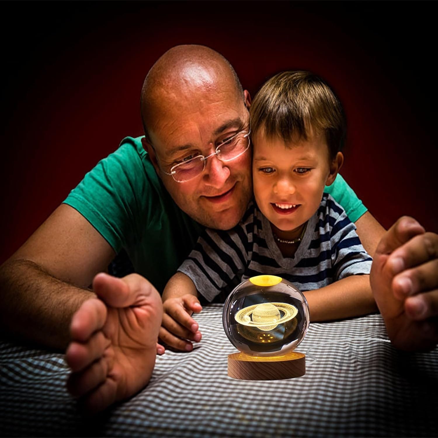 A man and a child smile while looking at a small levitating Saturn model on a table.