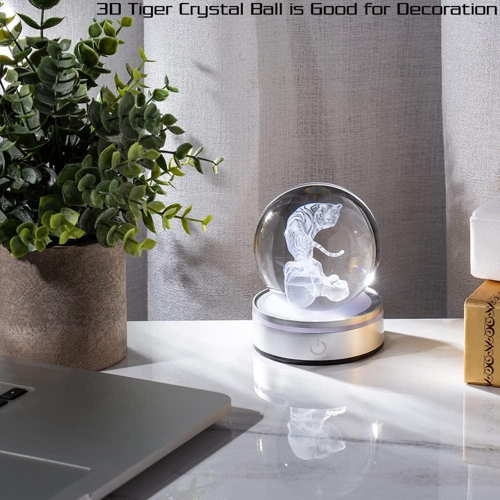 A 3D tiger crystal ball sits illuminated on a desk near a potted plant and a laptop.