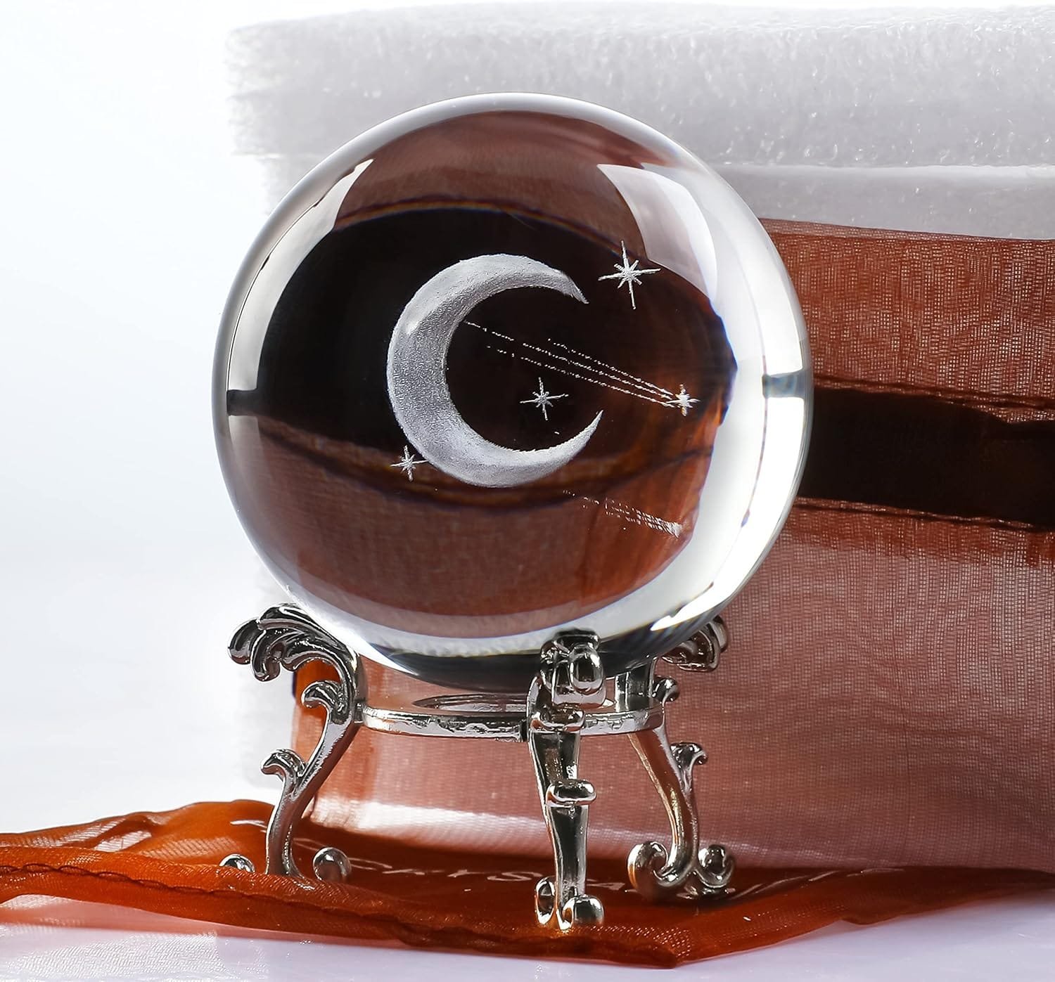 Crystal ball on a decorative stand, featuring a crescent moon and stars design, placed next to a brown box.