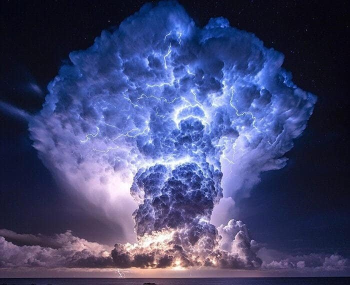 Dramatic cloud formation illuminated by lightning over a dark ocean horizon at night, as gamma-ray emissions subtly dance in the distant sky.