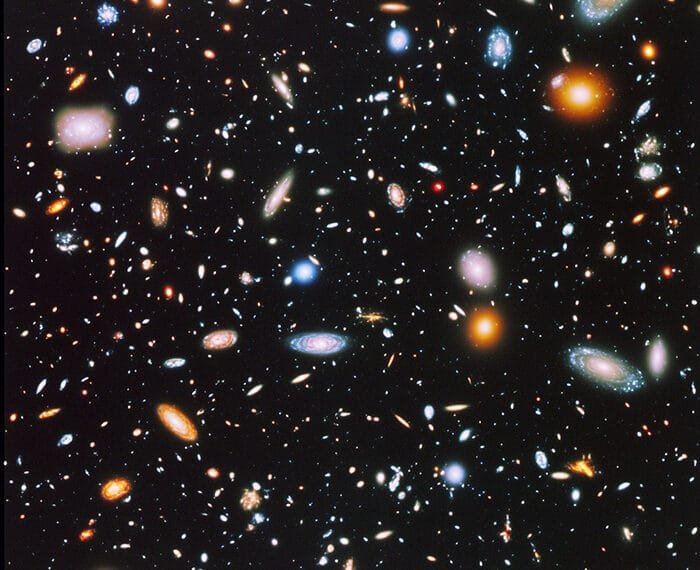 Colorful galaxies, a testament to cosmology, are scattered across a dark space background, featuring spirals and elliptical shapes that vary in size and brightness.