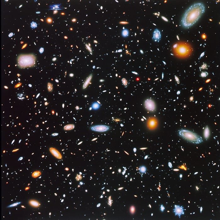 Colorful galaxies, a testament to cosmology, are scattered across a dark space background, featuring spirals and elliptical shapes that vary in size and brightness.