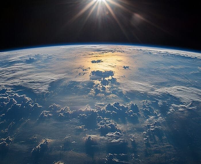 Sunrise over Earth's horizon as seen from space, illuminating clouds and ocean below. This breathtaking view of our Earth from space captures the serene beauty of our planet awakening to a new day.