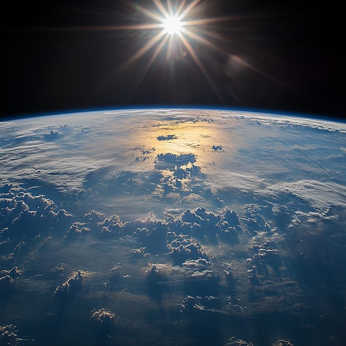 Sunrise over Earth's horizon as seen from space, illuminating clouds and ocean below. This breathtaking view of our Earth from space captures the serene beauty of our planet awakening to a new day.