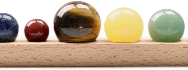 A wooden base holds a row of nine spherical stones of varying sizes and colors, including clear, red, brown, yellow, green, blue, and purple.