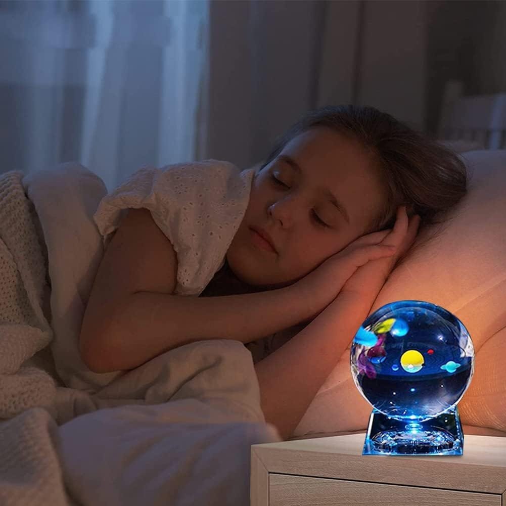 Child sleeping peacefully with hands under head, next to a glowing globe lamp on a bedside table.