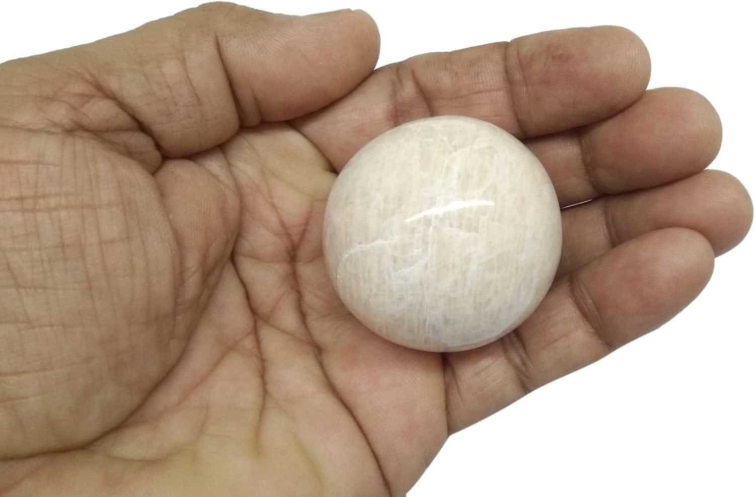 A hand holding a smooth, round, white stone.