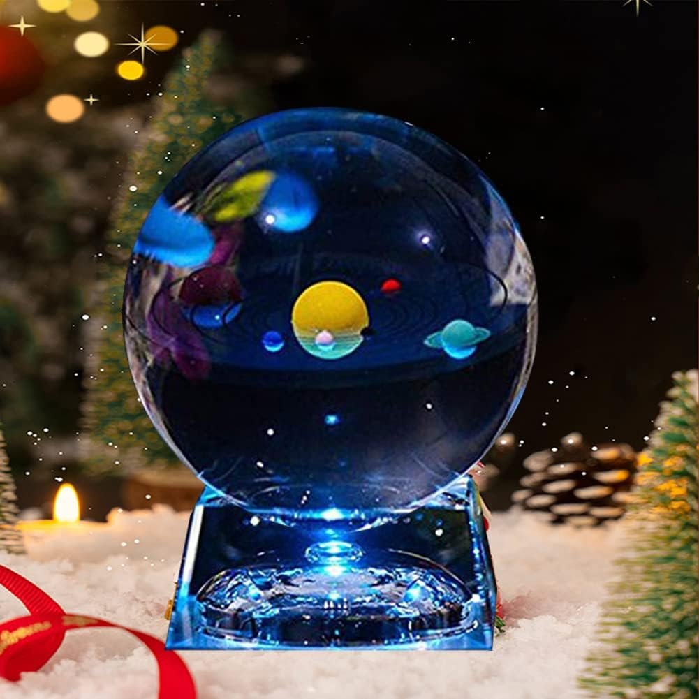 A glass sphere with colorful planets inside sits on a lit base surrounded by snow and holiday decorations.