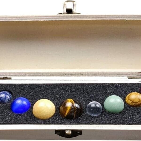 A wooden box containing eight marbles of various colors and materials, arranged in a row on black foam padding.