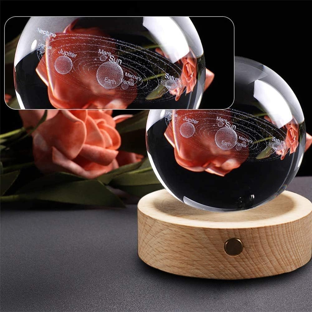 Crystal ball with solar system engraving, placed on a wooden stand. Reflected roses are visible in the background.