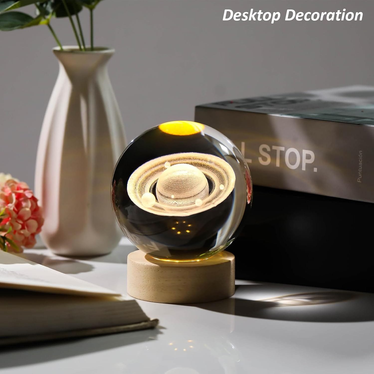 Glass orb with planet design on a wooden base, next to books and a vase with flowers on a table.