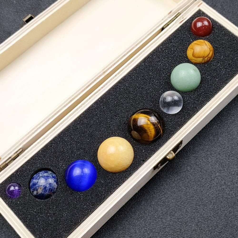 A wooden box with a black foam interior holding nine polished spherical stones in various colors and sizes.