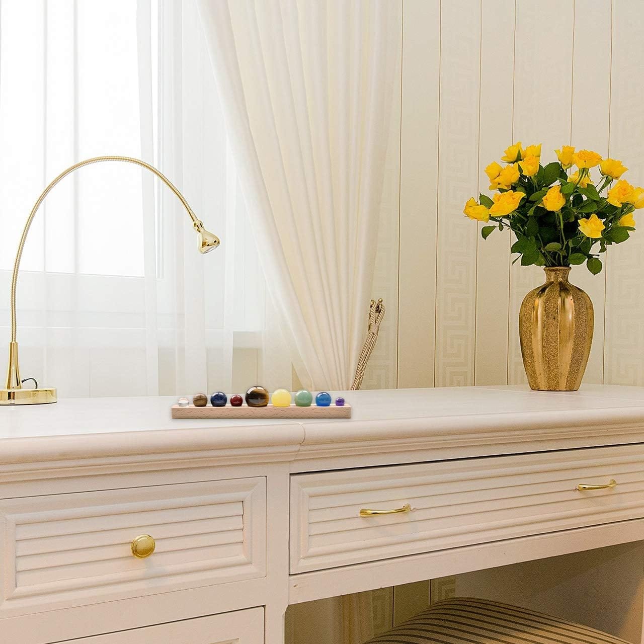 Elegant white desk with drawers, gold lamp, and a vase of yellow roses. A tray with colorful decorative spheres is set on the desk.