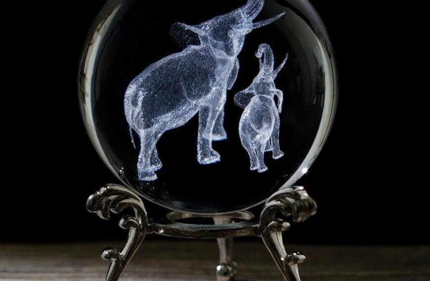 Glass orb with laser-etched elephants, mounted on an ornate metallic stand against a dark background.