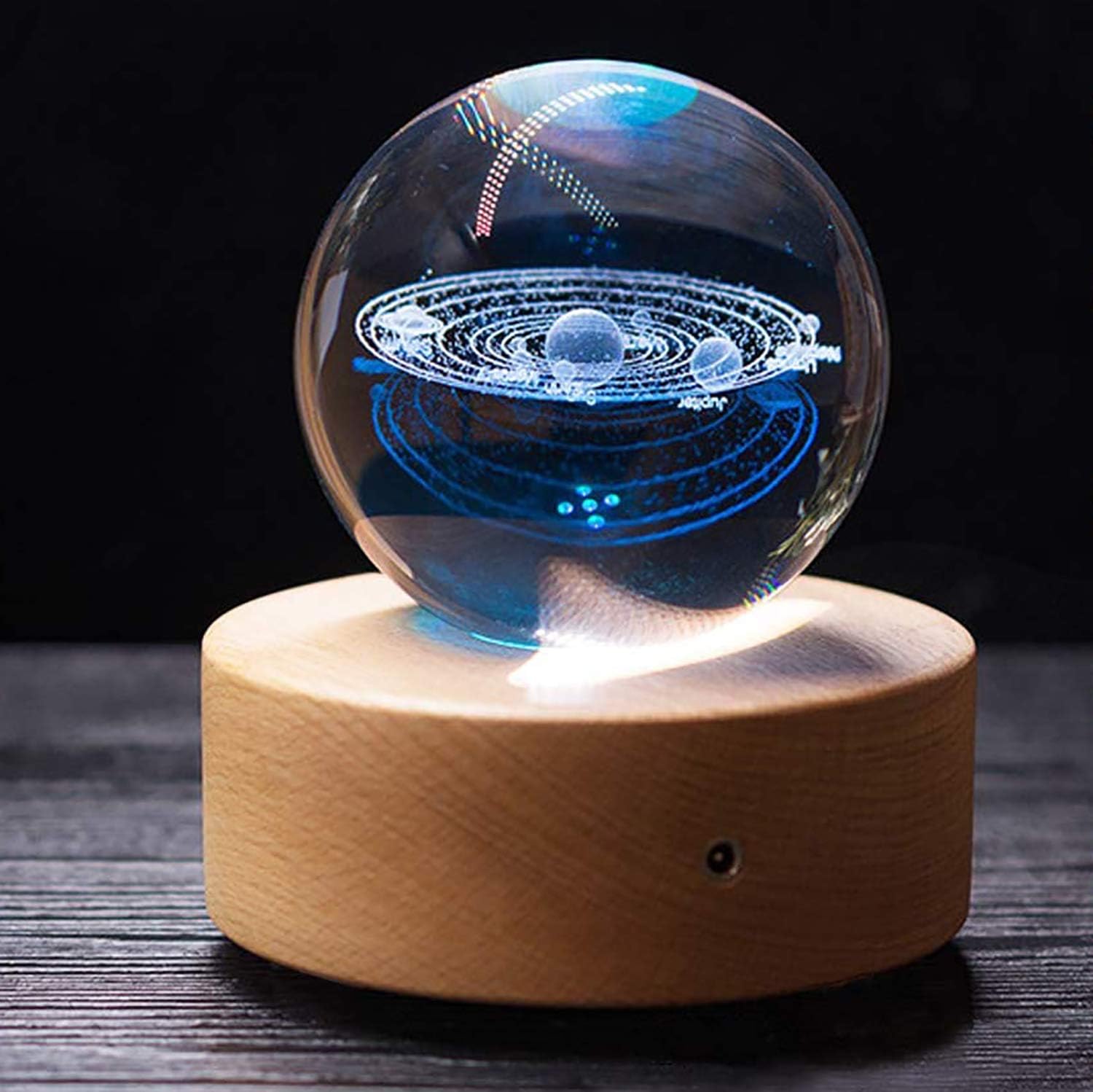 A transparent crystal ball with a blue solar system design sits on a round wooden base.