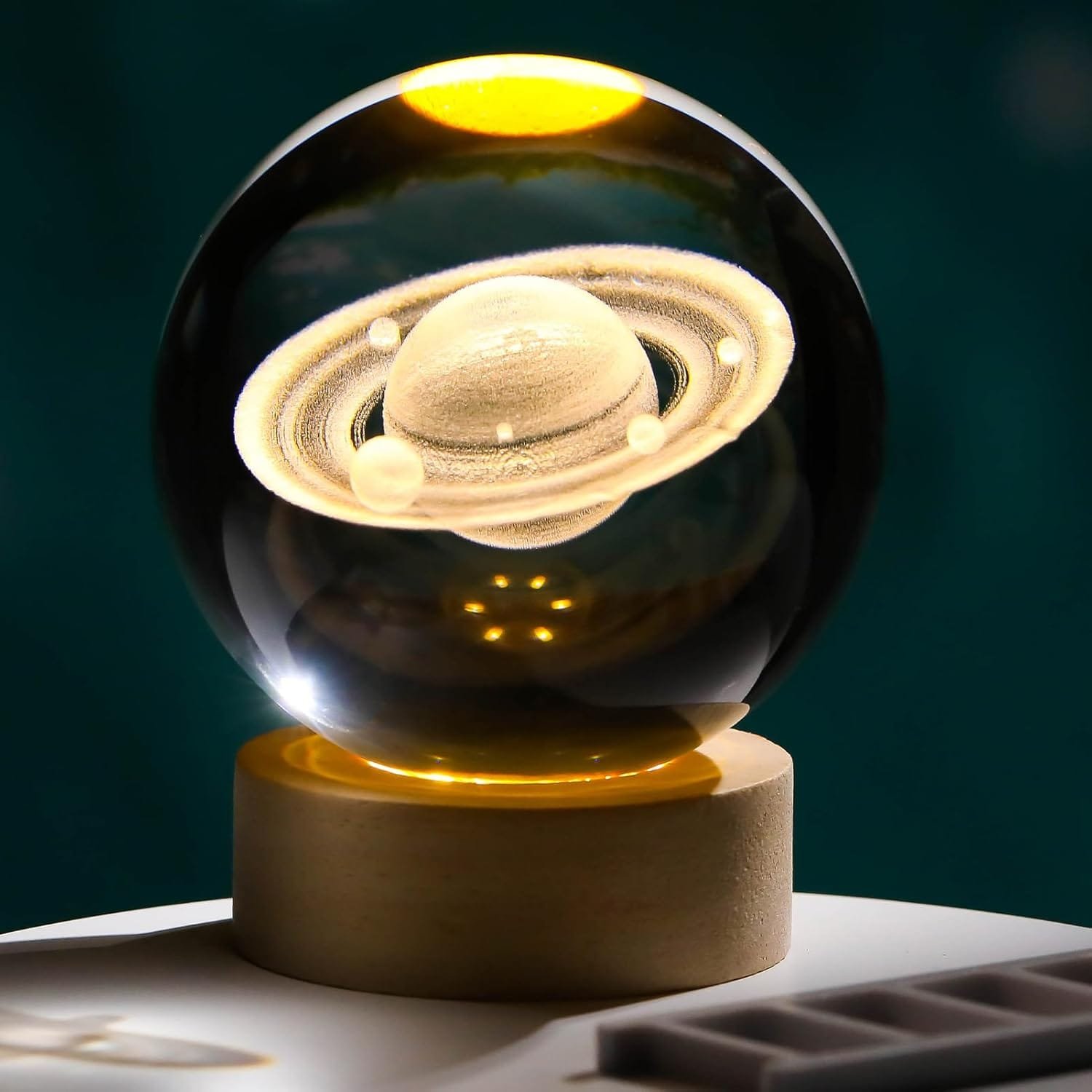 A glass orb with an intricate Saturn model inside, resting on a wooden base, illuminated from above.