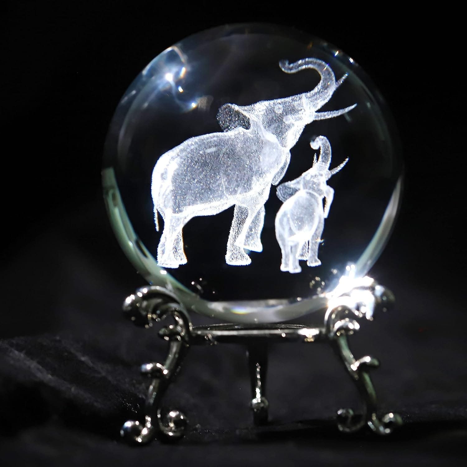 A glass orb on a decorative stand features etched images of an adult and baby elephant.