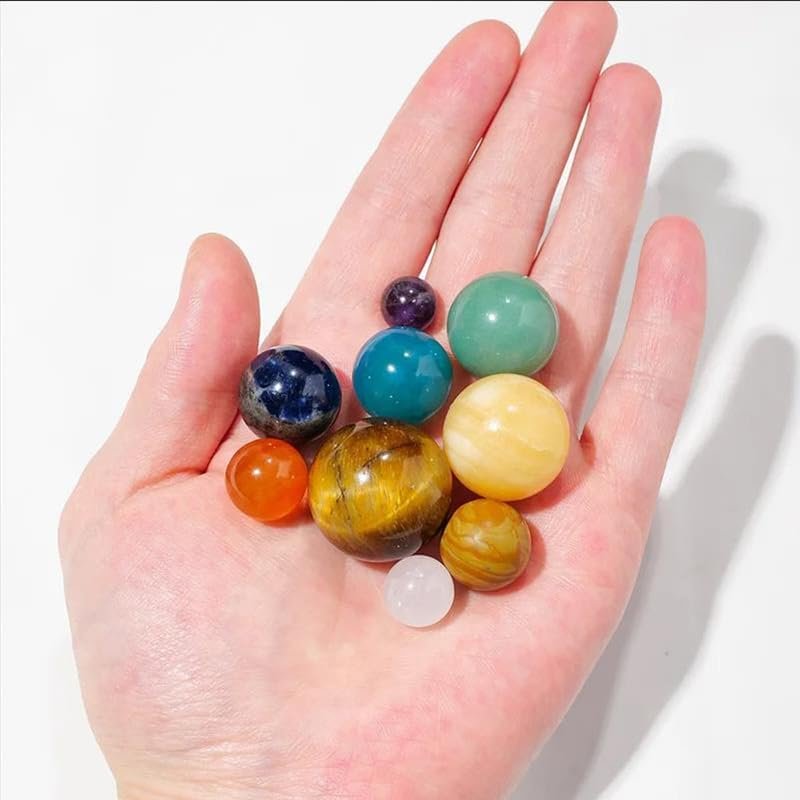 A hand gently holds ten vibrant gemstone spheres in different sizes, known as Chakra Healing Crystal Sphere Balls by Celestial Gifts, displayed against a spotless white backdrop.