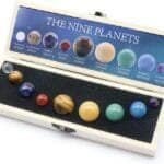 A Chakra Healing Crystal Sphere Ball by Celestial Gifts set includes nine planet-labeled spheres, symbolizing the solar system, housed in a wooden box with a foam insert.