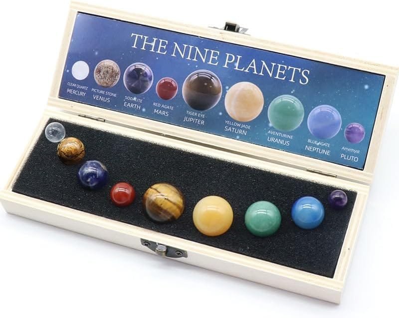 A Chakra Healing Crystal Sphere Ball by Celestial Gifts set includes nine planet-labeled spheres, symbolizing the solar system, housed in a wooden box with a foam insert.