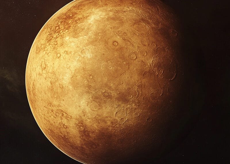 A textured, reddish-brown planet resembling Venus with visible craters and surface details, set against a dark background.