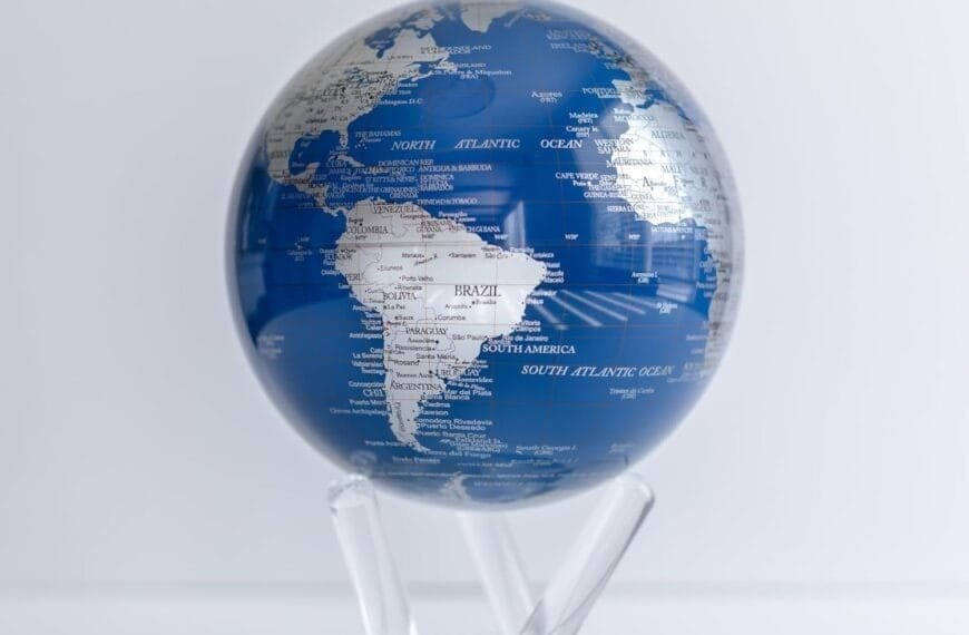The Globe Metallic 4.5" elegantly features parts of South America and the Atlantic Ocean, adorned in a striking blue and white design and perched on a clear stand.