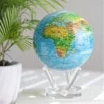 A *Globe Relief Map Blue 6"* sits on a clear stand beside a potted plant, showcasing regions of Africa, Europe, and the Atlantic Ocean in a well-lit room.