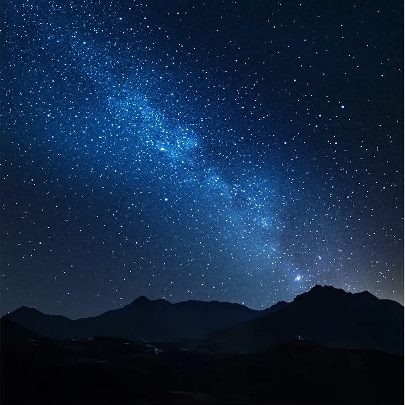 A starry night sky above a silhouette of mountain peaks, with countless stars forming the Milky Way visible across the horizon.