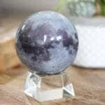 A spherical object with a lunar surface design is placed on a clear, geometric stand on a wooden surface.