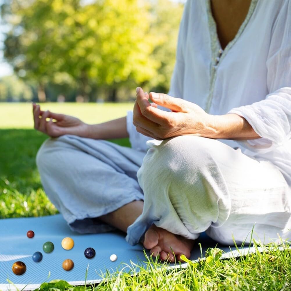 Person meditating on a blue mat in a park, wearing light clothing. Small spheres are arranged in front on the grass.