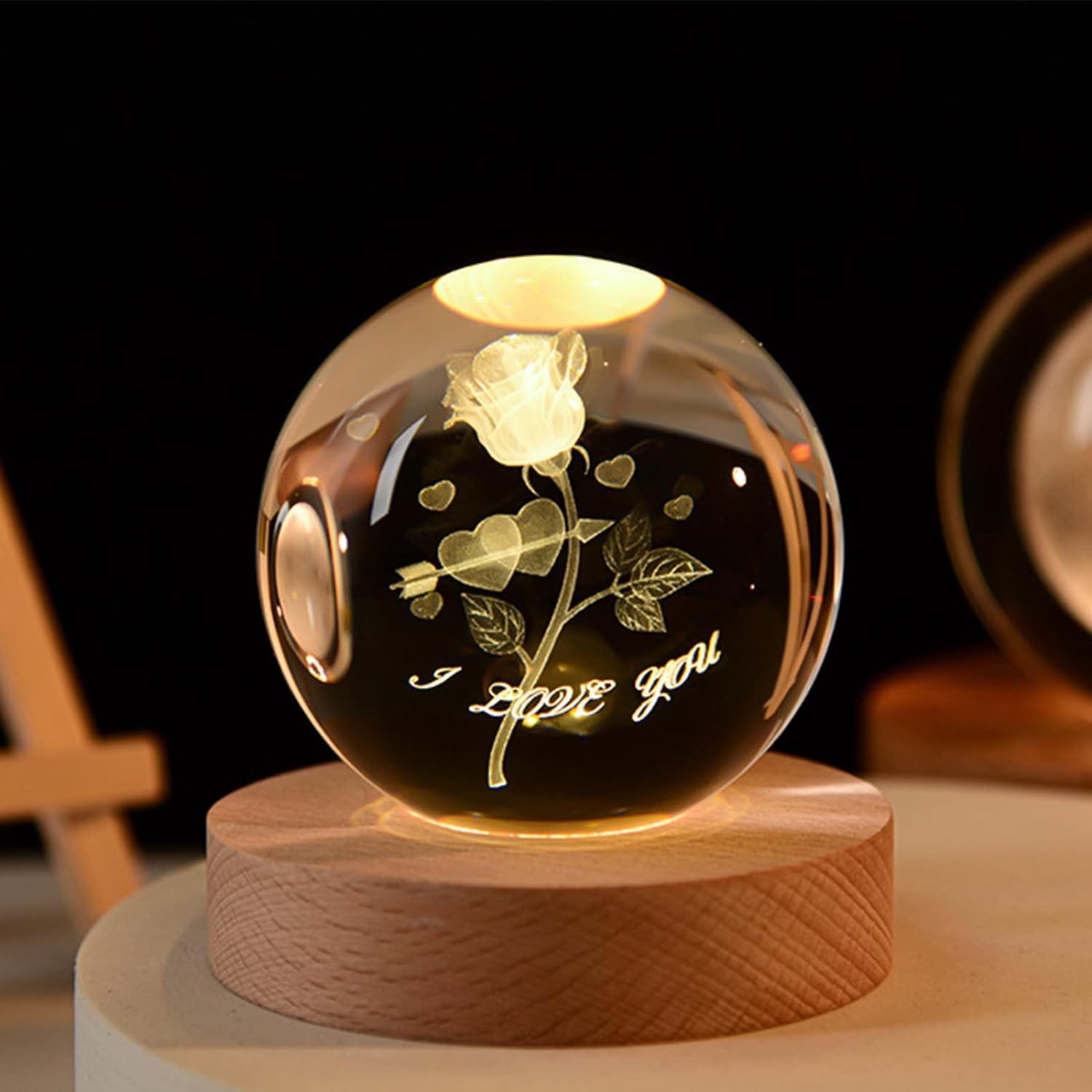 A glowing crystal ball on a wooden base displays an engraving of a rose, hearts, and the words "I love you.