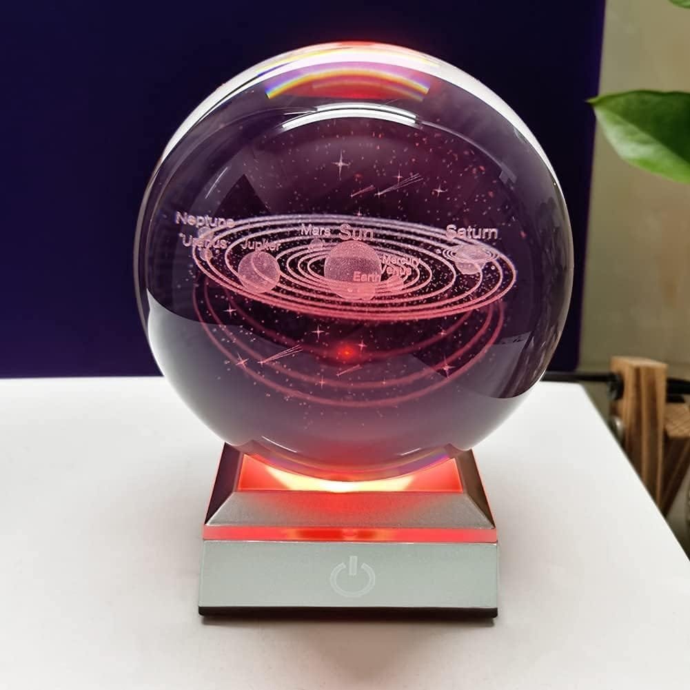 A glass globe etched with the solar system, showing planets and orbits, is placed on a lit base with a power button.