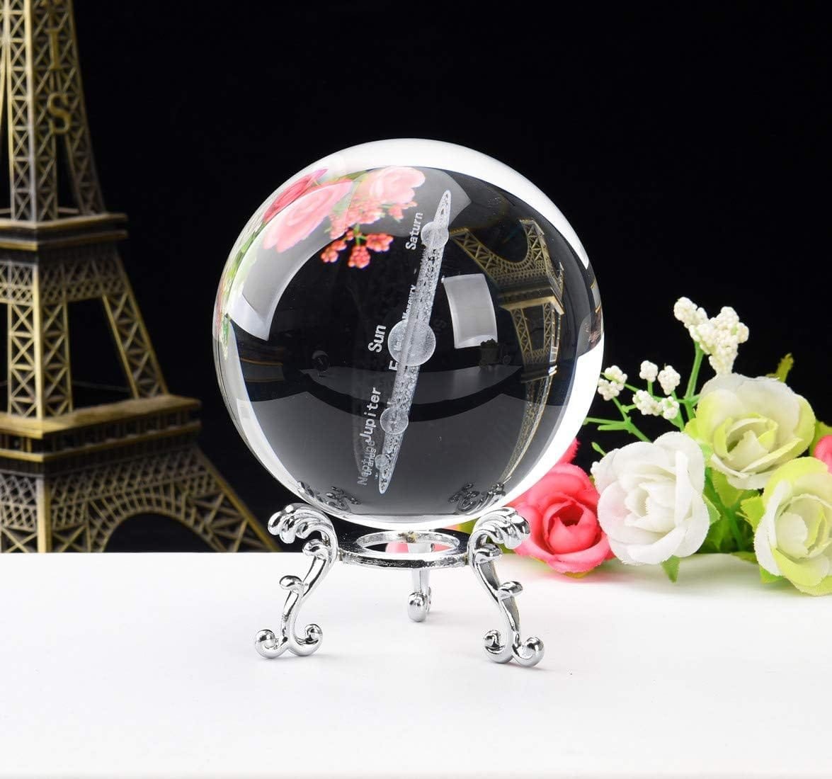 Glass orb with imprint of planets and flowers, on ornate metal stand. Eiffel Tower model and flowers in background.