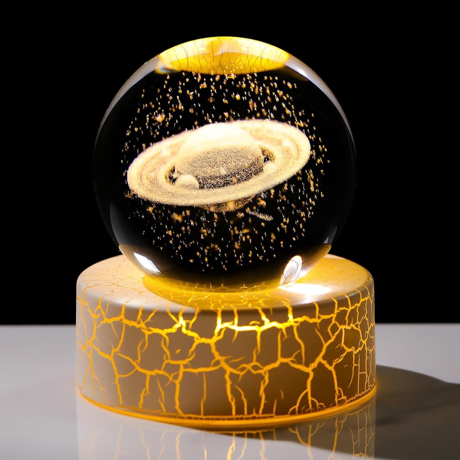 A glass sphere with a Saturn-like planet inside sits on a cracked, illuminated base, against a black background.