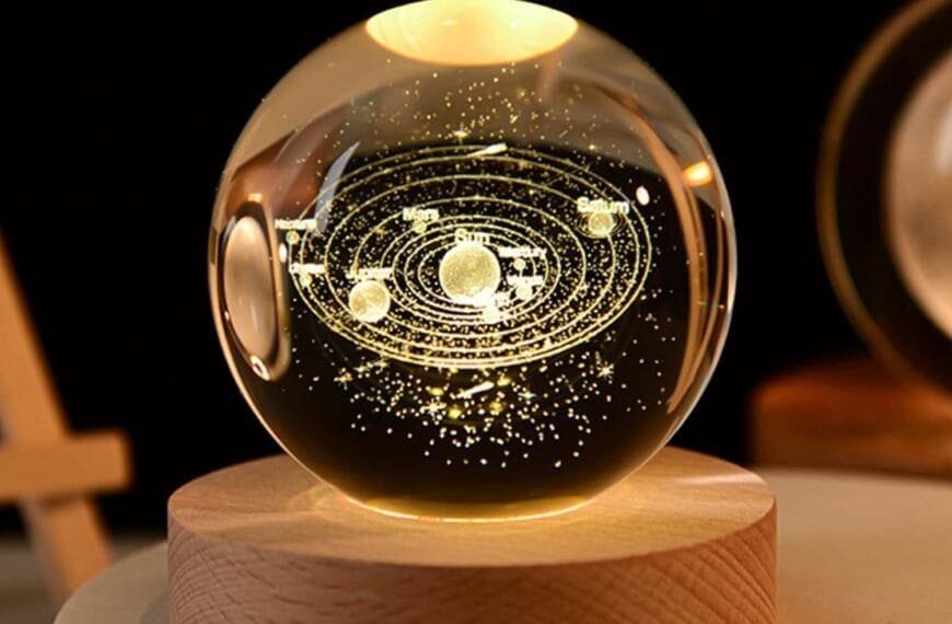 A glass orb with a glowing miniature solar system inside, resting on a wooden base.