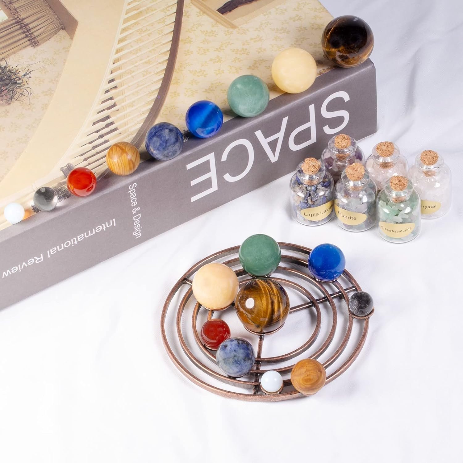 A book titled "SPACE" with colorful spheres on top, next to a round metal stand with planets and small jars filled with cork stoppers and labeled contents.