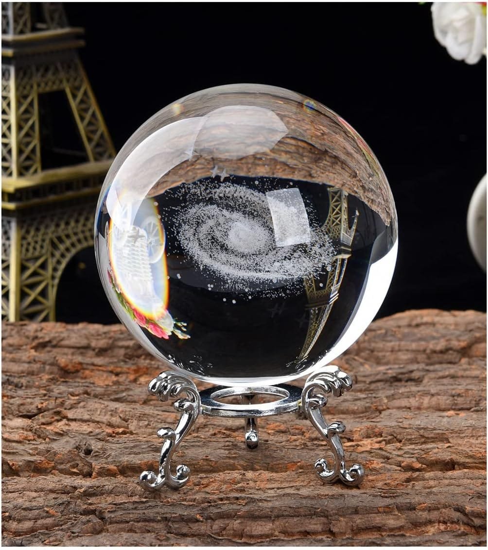 A glass orb with a spiral galaxy design inside, placed on an ornate metal stand. Eiffel Tower model in the background.