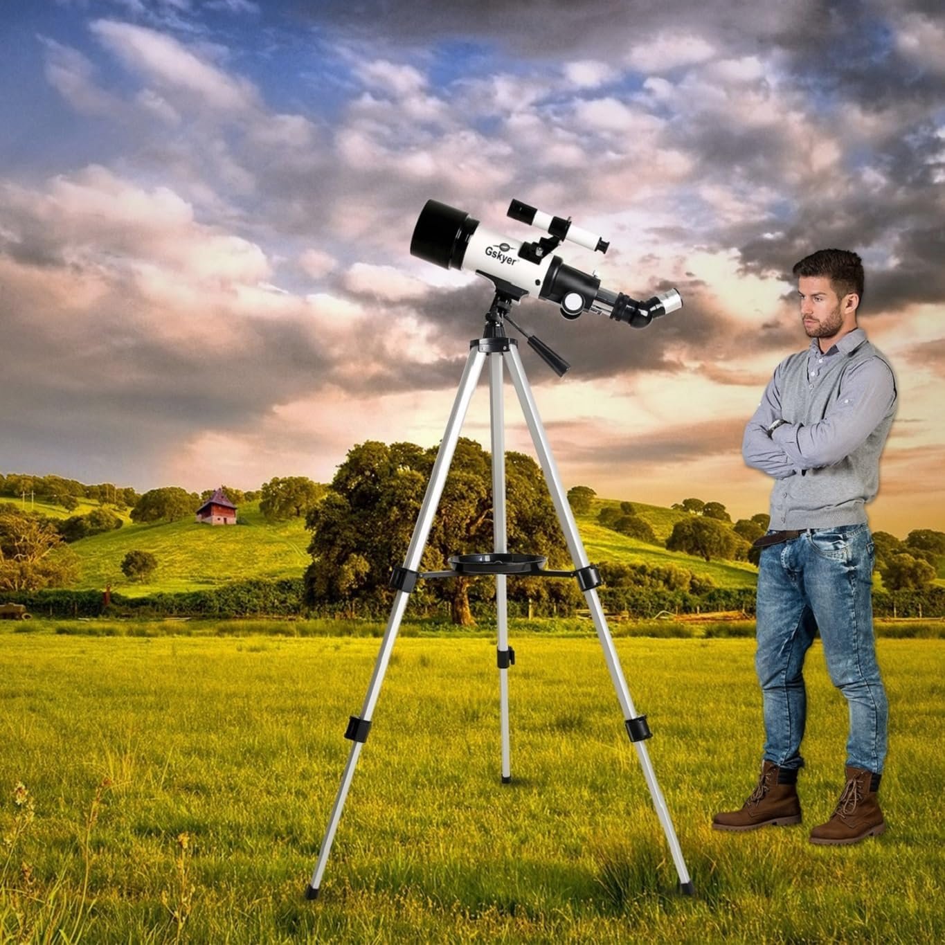 A man standing in a field, looking at a telescope on a tripod. Hills and a cloudy sky are in the background.